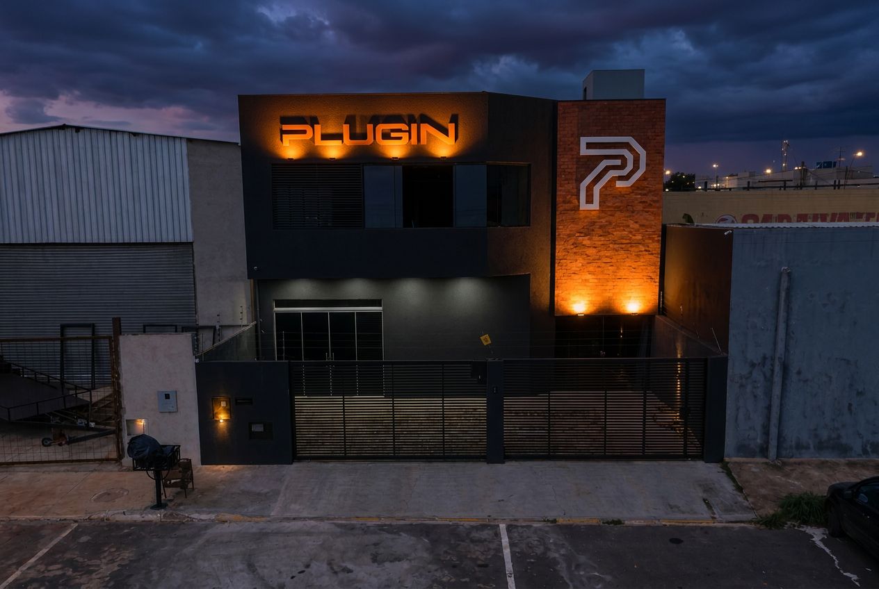 Fachada da sede da Plugin ao entardecer, com o letreiro iluminado em laranja